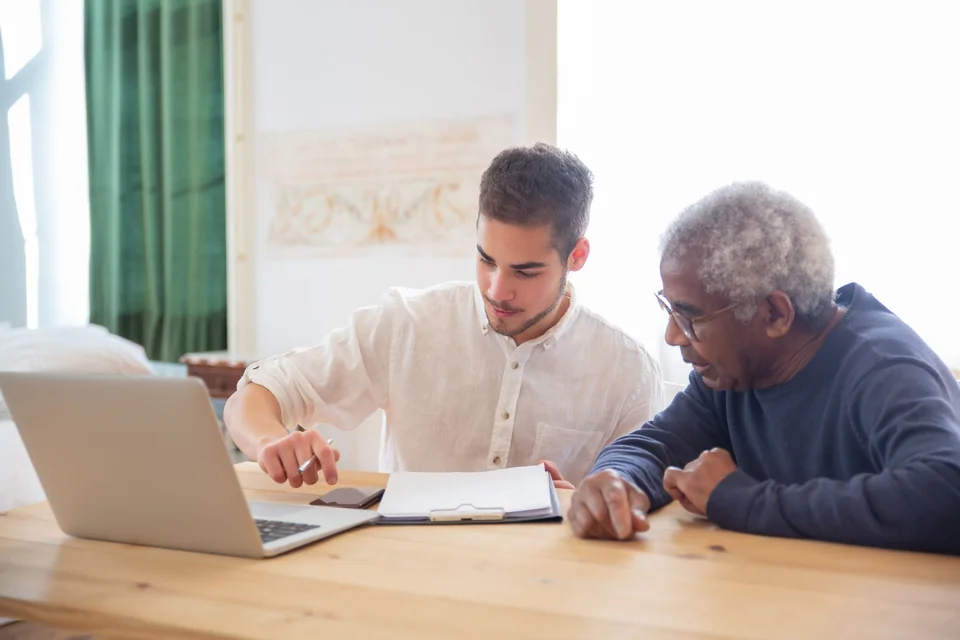 A support worker sitting beside an older man at a table, going through paperwork with him.