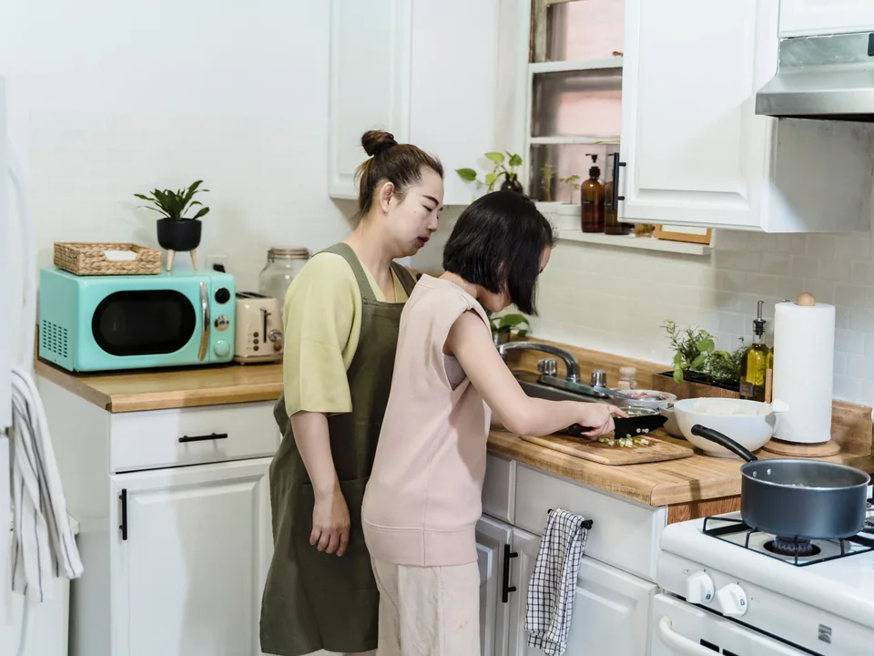 A support worker and a young person preparing food together at a kitchen bench in a bright home.